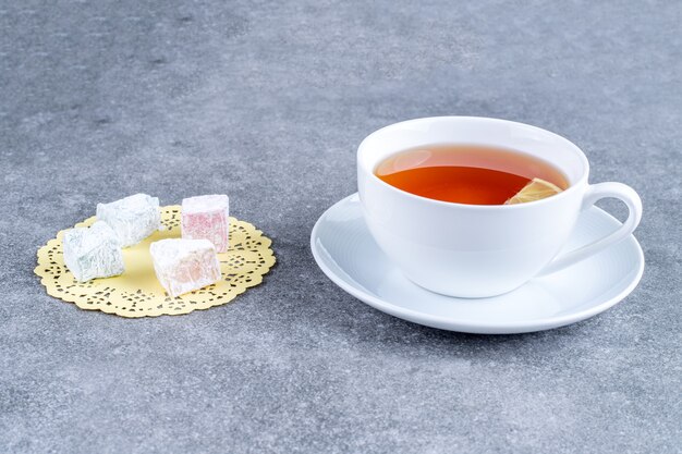 Cup of tea and soft candies on marble surface