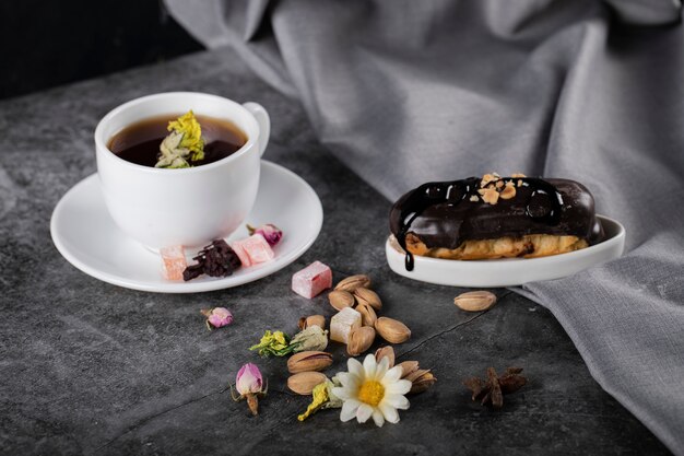A cup of tea with chocolate eclair decorated with blossoms and nuts
