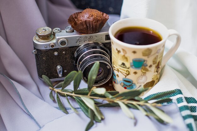 A cup of tea with a chocolate praline and a photo camera.
