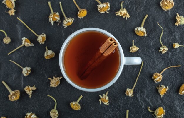 Cup of tea with cinnamon and pile of dried chamomiles.