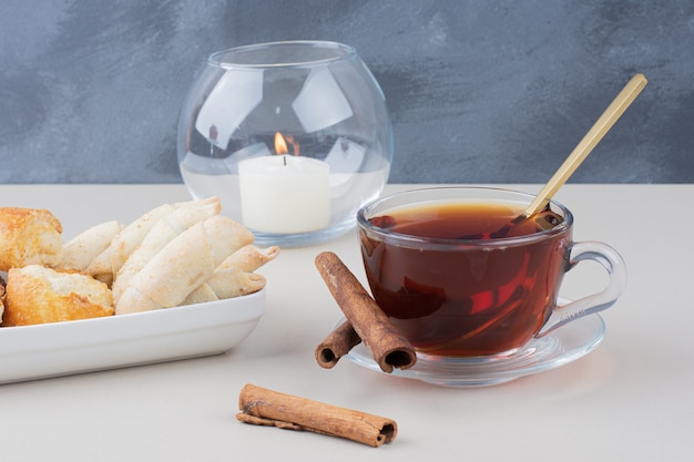 Чашка чая с корицей и печеньем на белом столе.