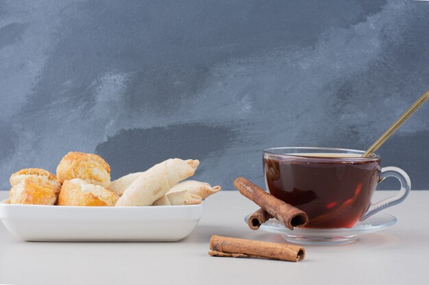 A cup of tea with cinnamons and cookies on white table.