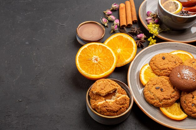 cup of tea with cookies and fresh sliced oranges on dark