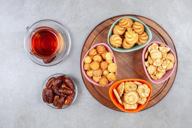 A cup of tea with dates next to assortment of cookies on a wooden board on marble background. High quality photo