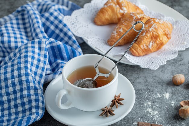 Cup of tea with delicious croissants on marble surface.