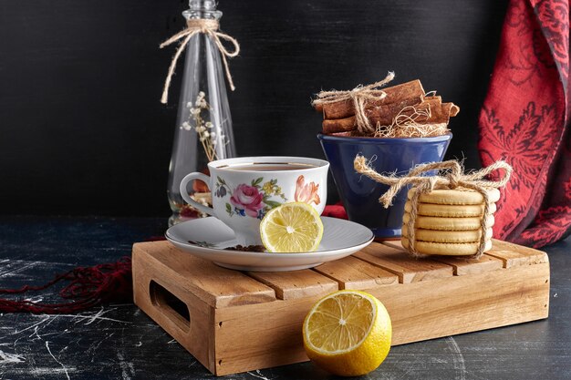 A cup of tea with lemon, cinnamon and cookies. 