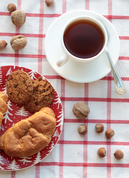 A cup of tea with nuts and pastries on the checked tablecloth. Top view.
