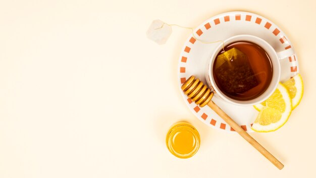 Cup of tea with organic lemon slice and honey on beige backdrop