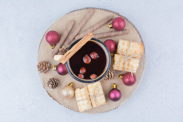 Cup of tea with rosehips, cookies and baubles on wooden board. 