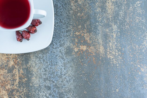 Cup of tea with rosehips on marble background.