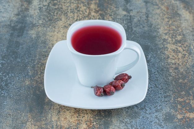 Cup of tea with rosehips on marble background.