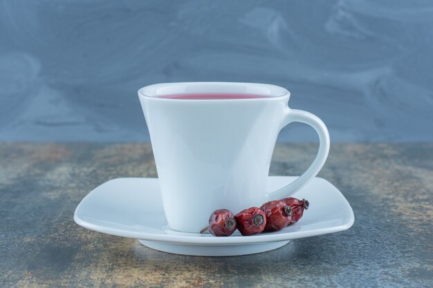 Cup of tea with rosehips on marble table.