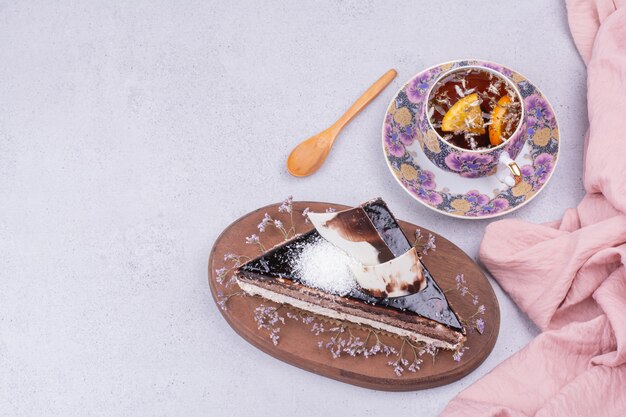 A cup of tea with a slice of chocolate cake on grey surface