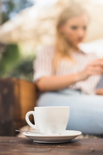 Cup of white coffee with saucer and spoon on wooden table