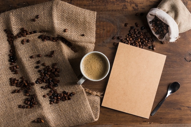 Cup with cardboard near sack with coffee beans and sackcloth