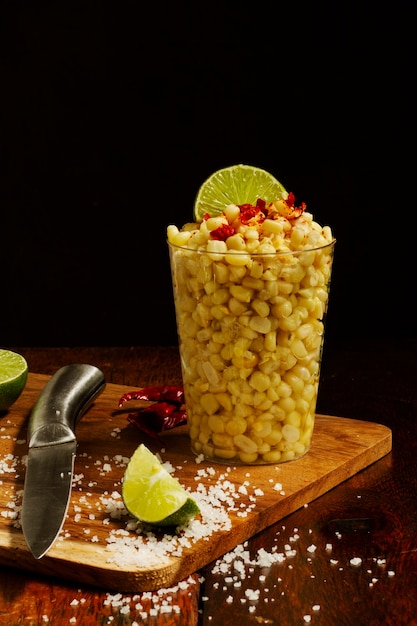 Cup with delicious esquites on wooden board