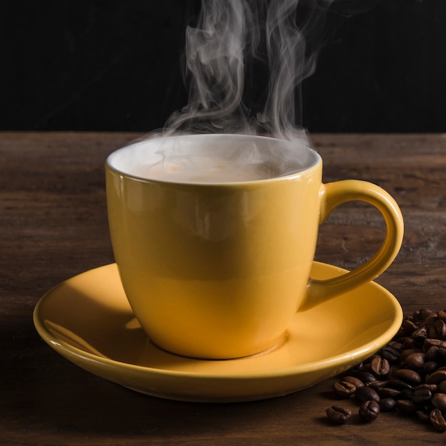 Чашка с горячим напитком возле кофейных зерен