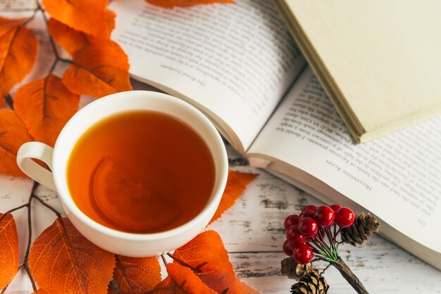 Cup with lemon tea and book among autumn leaves