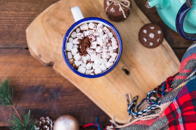 Cup with marshmallow near biscuits and scarf