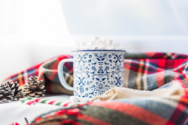 Cup with marshmallow near scarf and fir snags 