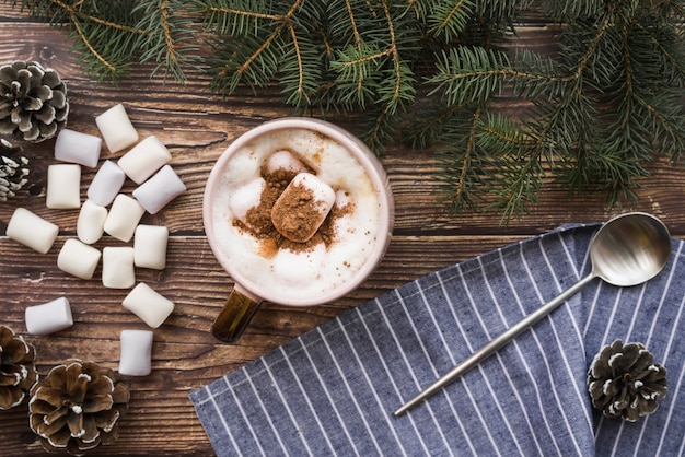 Cup with marshmallows near spoon, fir twigs and snags 