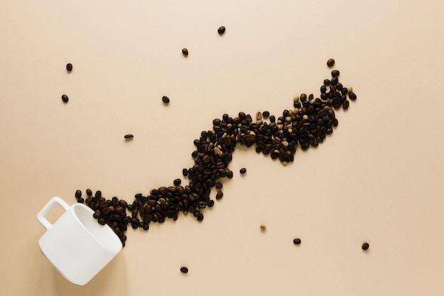 Cup with spilled coffee beans on beige table