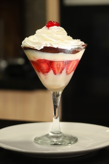 A cup with a strawberry dessert with cherry, whipped cream and chocolate (sobremesa de morango na taãâãâ§a) Premium Photo
