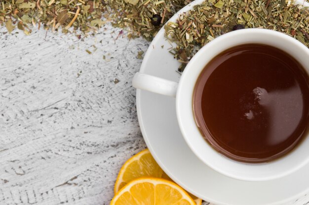 Cup with tea with lemon and dry herbs on wooden background