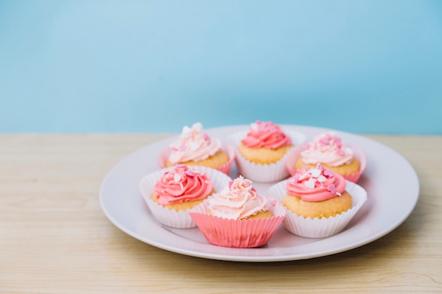 Cupcake with cream and sprinkle on white plate over the wooden desk against blue backdrop