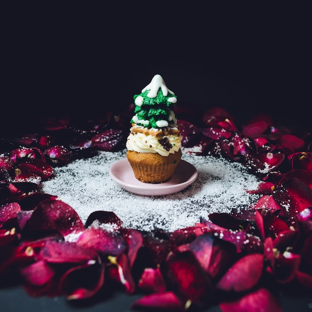 バラの花びらの輪の上に立つ釉薬の冬の木を持つカップケーキ