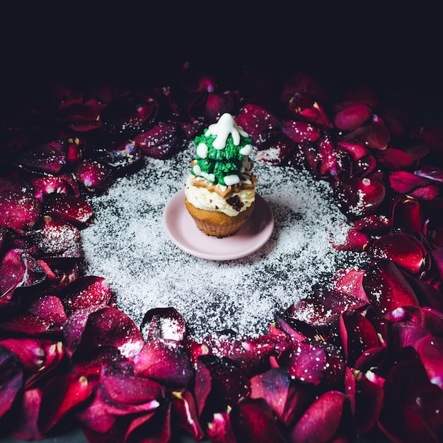 Cupcake with glaze fir tree on top stands in the circle of rose petals