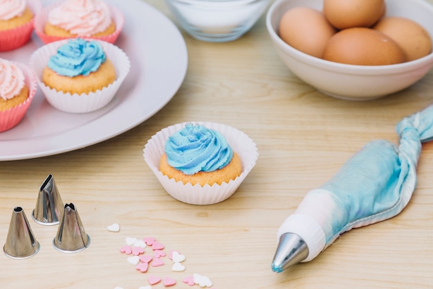Cupcake with icing bag; sprinkle; nozzle on wooden desk