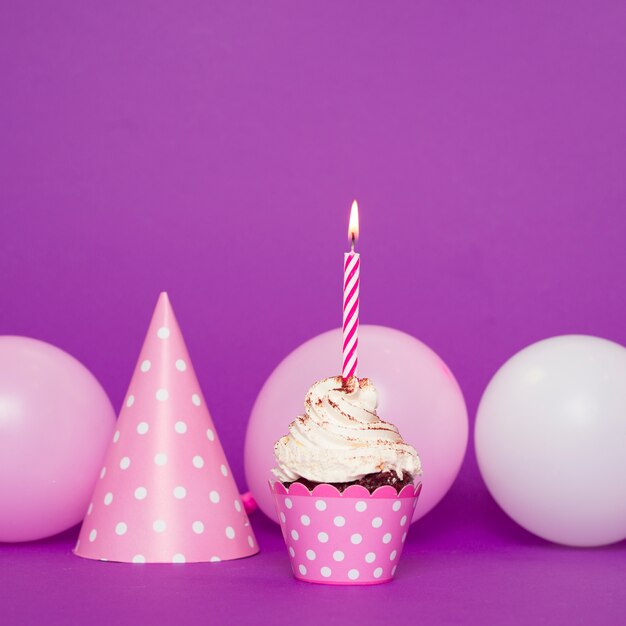 Cupcake with lit candle next to hat