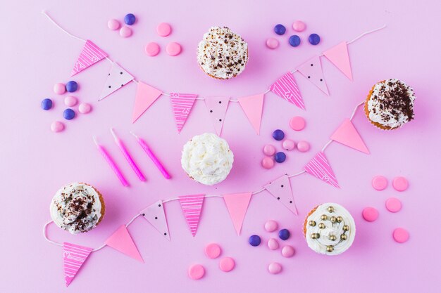 Кексы; конфеты; свечи и овсянка на розовом фоне