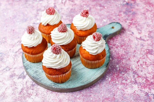 Cupcakes decorated whipped cream and frozen raspberries.