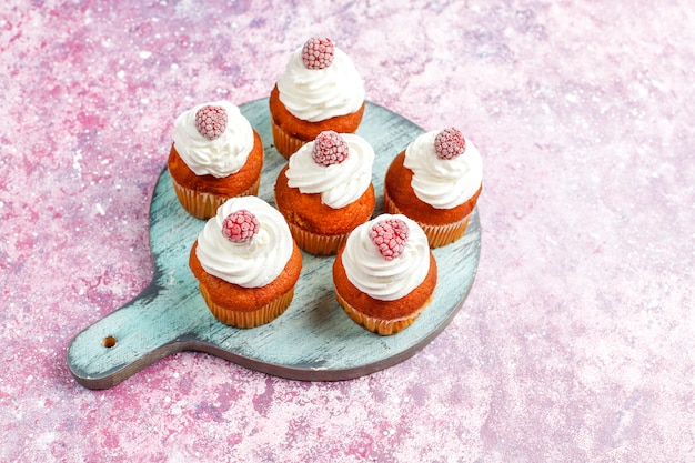 Free photo cupcakes decorated whipped cream and frozen raspberries.