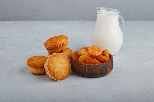 Cupcakes e albicocche secche con un barattolo di latte su sfondo grigio.