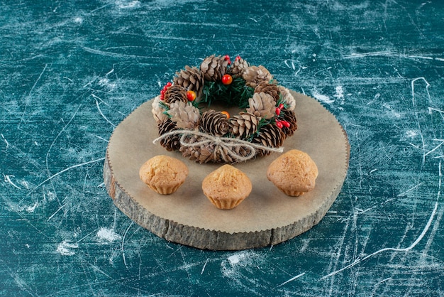 Cupcakes and a pine wreath arranged on a wooden board on blue.