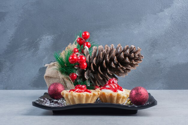 Cupcakes with strawberry sauce on a black platter, bundled with christmas ornaments on marble surface