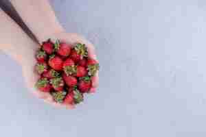 Free photo cupped hands holding a heap of strawberries on marble background. high quality photo