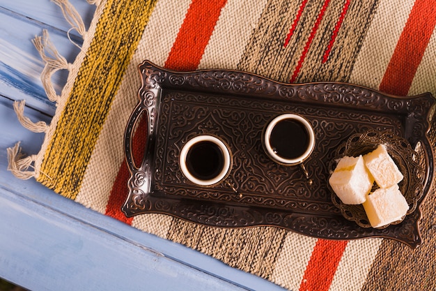 Cups of coffee near saucer with sweet Turkish delights on tray against mat