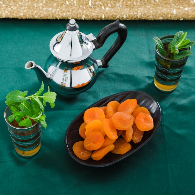 Cups of drink near teapot and dried apricots 