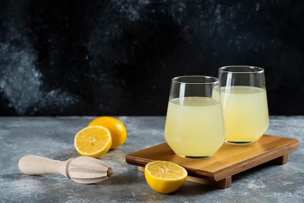 Cups full of lemonade with slices of lemon and wooden reamer.