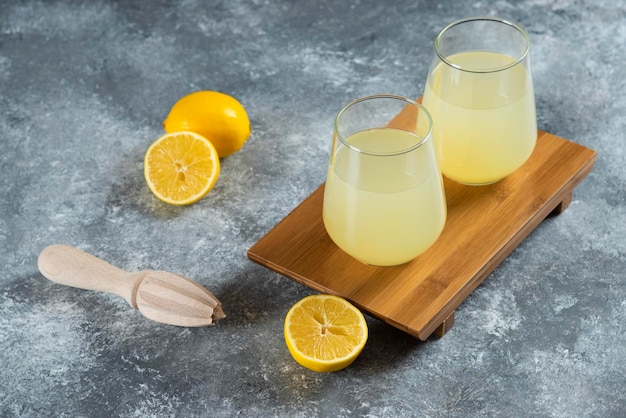 Cups full of lemonade with slices of lemon and wooden reamer.