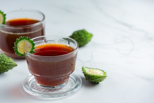 cups of hot bitter gourd tea with raw sliced bitter gourd on white marble floor