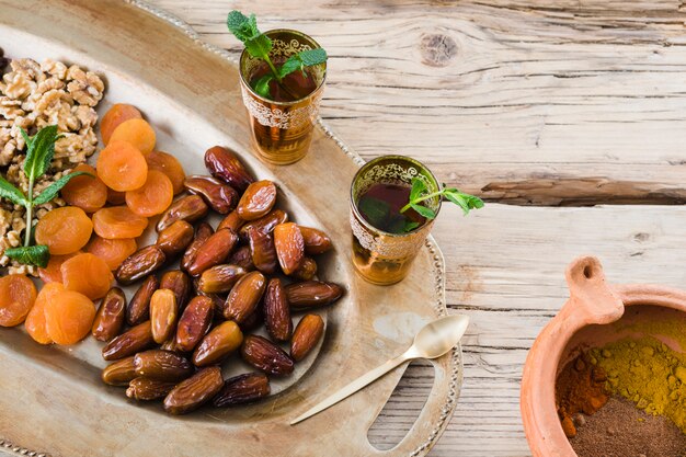 Cups with plant twigs near bowl with spices and dried fruits and nuts on tray