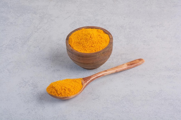 Curcumin powder in a wooden spoon on concrete background.