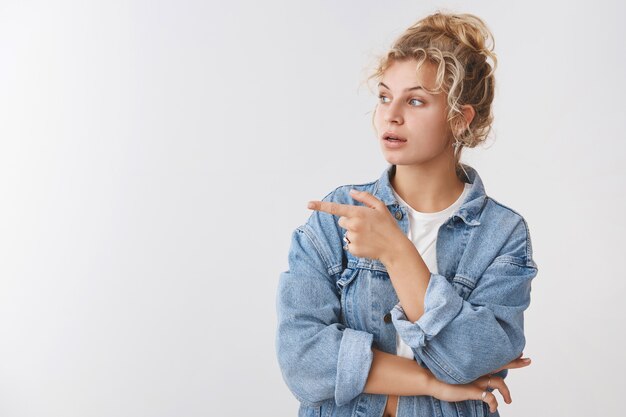 Curious attractive female blond customer pick furniture asking advice shop assistant turn point left interested questioned gazed sideways intrigued what happening, posing white wall