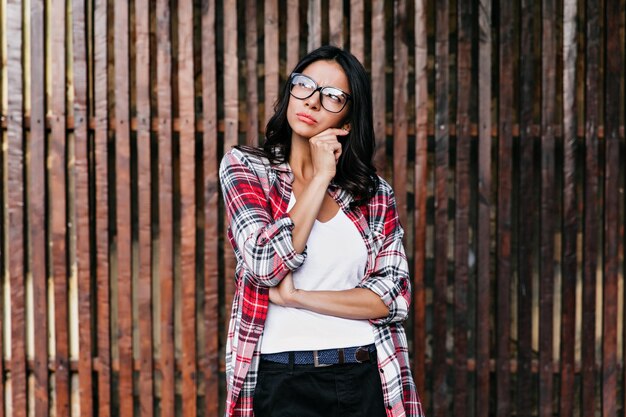 Curious blackhaired girl looking up while posing on wooden background Outdoor photo of joyful latin lady thinking about something