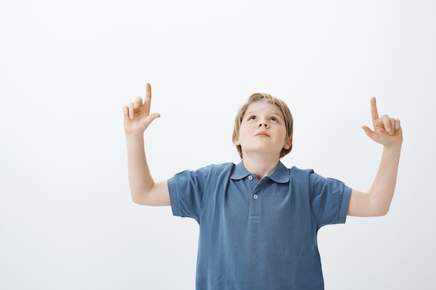 Бесплатное фото Любопытный беззаботный белокурый мальчик в синей футболке, поднимает руки, смотрит и указывает вверх указательными пальцами, наслаждается красивыми звездами и задает вопрос маме